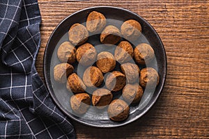 Chocolate truffles covered with cocoa powder on plate on wooden table. Top view