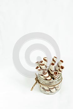 Chocolate Wafer rolls in Glass Jar on White background Copy space