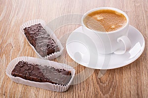 Chocolate wafers in paper wrapper, cup of coffee on saucer on table