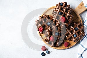 Chocolate waffles and berries on a wooden plate on a wooden background. Top view and copy space