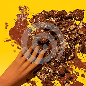 Chocolate waffles trash and fake hand on yellow background. Sweets and cacao lover concept. Minimal art. Holidays party time,