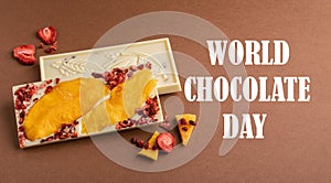Chocolate white fruit whole tile decorated with slices of fruit nuts on a brown background. Text World Chocolate Day