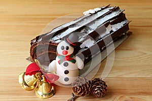 Chocolate Yule Log Cake or Buche de Noel Decorated with Snowman Marzipan and Dry Pine Cones, Christmas Ornament on Wooden Table