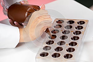 Chocolatier pouring caramel filling into chocolate mold preparing handmade candy photo