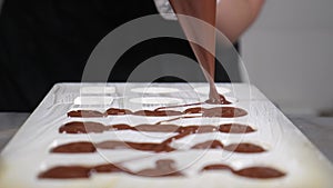 Chocolatier pouring melted chocolate into molds in pastry shop. Tempering chocolate. Craft sweets candies cooking