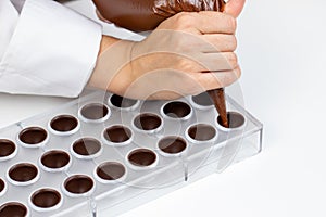 Chocolatier pouring praline filling into chocolate mold preparing belgium candy photo