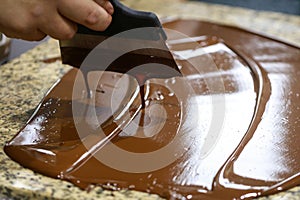 Chocolatier with a spatula is stirring the tempered liquid chocolate on a granite table