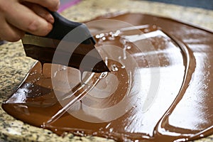 Chocolatier with a spatula is stirring the tempered liquid chocolate on a granite table