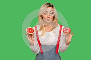 Choice between healthy eating vs junk food. Portrait of pensive adult woman holding doughnut