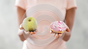 Choice of healthy or junk food. Closeup view of black woman choosing between donut and apple on light background