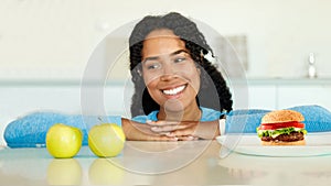 Choice between healthy and unhealthy food. African american woman looking at apple choosing between fruits and junk food