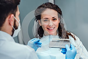 Choice of tooth color with a special scale. Dentist select a shade of tooth enamel for the young pretty girl of the patient.