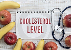 Cholesterol Level text on paper with stethoscope, delicious red apple, measurement tape and blue dumbbell on wooden