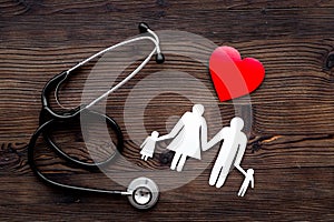 Choose family health insurance. Stethoscope, paper heart and silhouette of family on dark wooden background top view