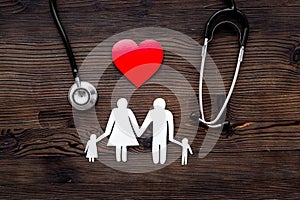 Choose family health insurance. Stethoscope, paper heart and silhouette of family on dark wooden background top view