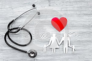 Choose health insurance. Stethoscope, paper heart and silhouette of family on grey wooden background top view