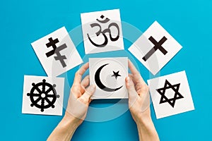 Choose religion concept. Hand with Islam crecent near world religions symbols on blue background top view photo