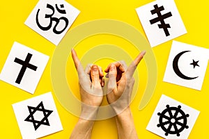 Choose religions concept. Hands point on Christianity, Catholicism, Buddhism, Judaism, Islam symbols on yellow photo