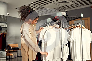 Choose what you like. Young woman looking at already made items in the store. Choosing clothes at custom T-shirt