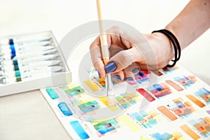 Choosing color for painting on paper with watercolor paints with female hand holding brush on colors palette background.