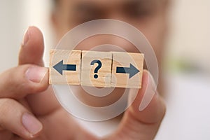 Choosing direction concept, man holding wooden block with arrow and question mark symbol