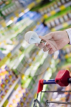 Choosing energy efficient lighting: closeup on male or female hand holding or selecting LED diode light bulb lamp in DIY store