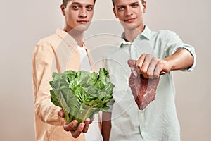 Choosing healthy eating. Two young caucasian twin brothers holding fresh green salad and piece of meat while standing