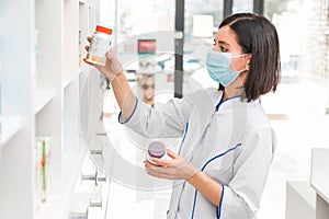 Choosing the right medicine. professional looking female pharmacist with medical mask on in drug store studying the