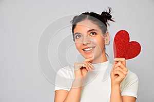 Choosing the right variant. portrait of woman holding a sparkling red heart valentine thinking while smiling