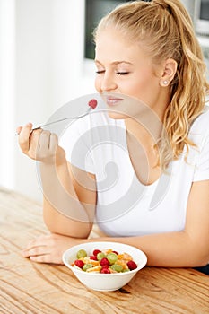 Choosing to follow a healthy diet. Attractive young woman eating fruit salad in her kitchen.