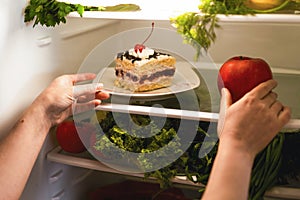 Choosing what to eat cake or apple. Food in the refrigerator. Adherence to a diet.