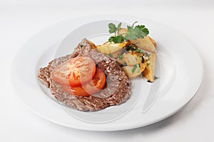 Chop steak with French fries tomato and parsley on a plate isolated