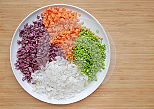 Chopped asparagus, carrot, radish and sweet purple potatoes on white plate against wooden background with copy space