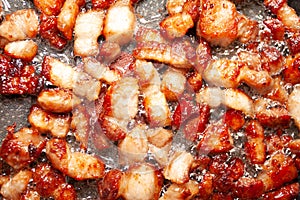 Chopped bits of bacon frying in a skillet