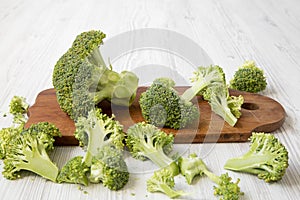 Chopped broccoli on a wooden cutting board on white wooden table, side view.