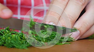 Chopped bunch of dill with knife on wooden kitchen board