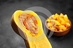 Chopped butternut squash, pumpkin half, fresh vegetable pieces in wooden bowl on black stone table