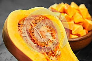 Chopped butternut squash  pumpkin half  fresh vegetable pieces in wooden bowl on black stone table