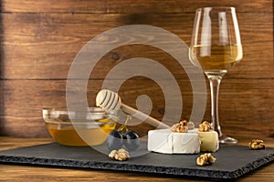 Chopped camembert cheese, nuts, honey and sweet grapes on the background of a glass of white dry wine