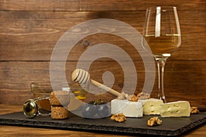 Chopped camembert cheese, nuts, honey, sweet grapes and cork from wine bottle on the background of a glass of white dry wine