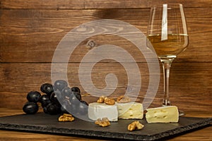 Chopped camembert cheese, nuts and sweet grapes on the background of a glass of white dry wine