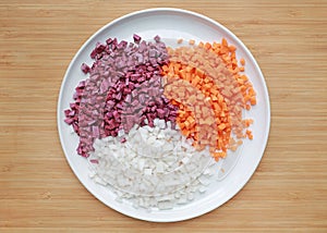 Chopped carrot, radish and sweet purple potatoes on white plate against wooden background