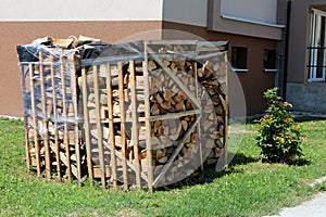 Chopped firewood stacked in leaning wooden frames and prepared for cold winter days in front of newly renovated apartment building