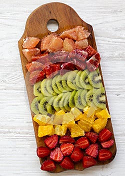 Chopped fresh fruits arranged on cutting board on white wooden surface, top view. Ingredients for fruit salad. From above, flat