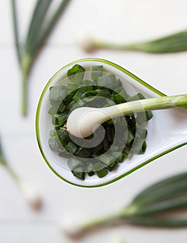 Chopped fresh green onions in spoon  on blurred background of whole onions. Top view