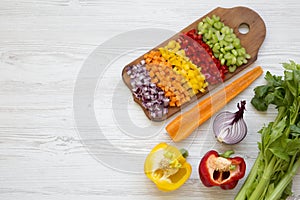 Chopped fresh vegetables arranged on cutting board on white wooden table, overhead view. Flat lay, from above, top view. Copy spa photo
