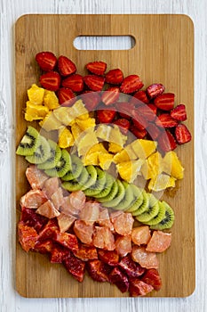 Chopped fruits arranged on cutting board on white wooden background, top view. Ingredients for fruit salad. From above, flat lay,