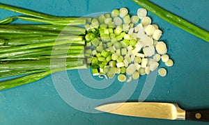 Chopped green onions or scallions on blue with knife
