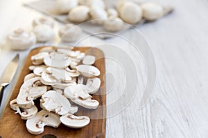 Chopped mushrooms on wooden chopping board over white wooden background, close-up. Side view.