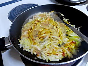 Chopped onions frying in a frying pan on a the stove with a bit of oil and some spices.